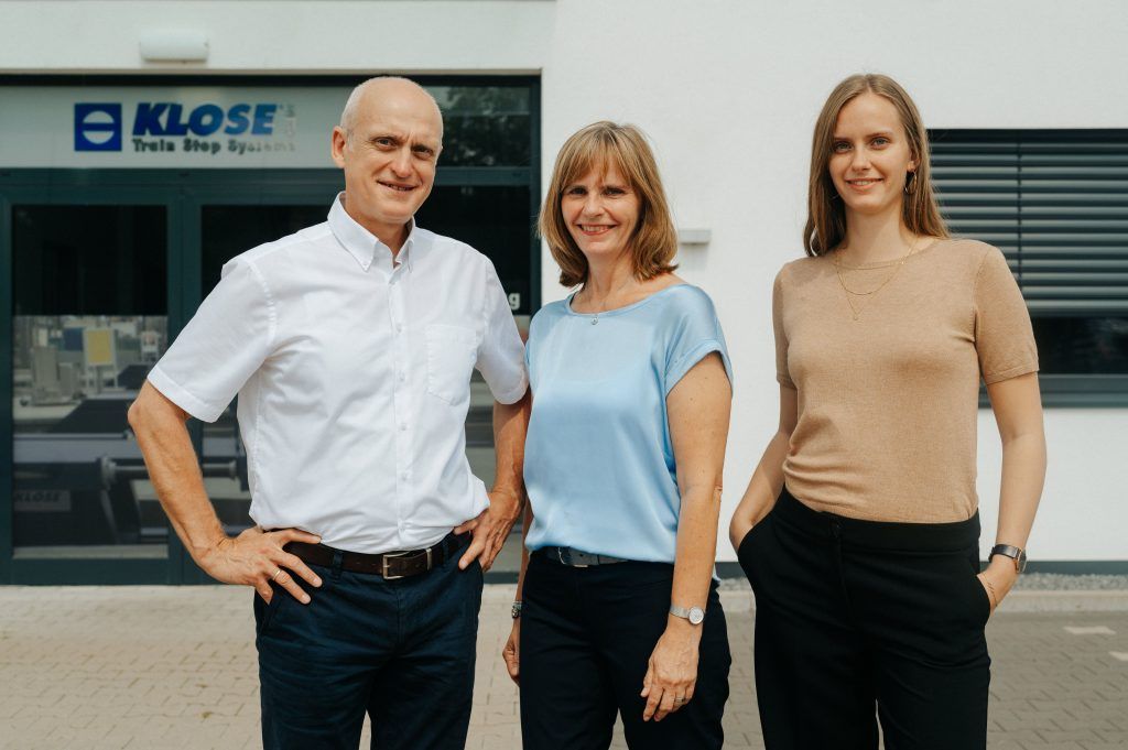 Frau und Herr Klose und ihre Tochter stehen vor Ihrem Unternehmen und schauen in die Kamera.